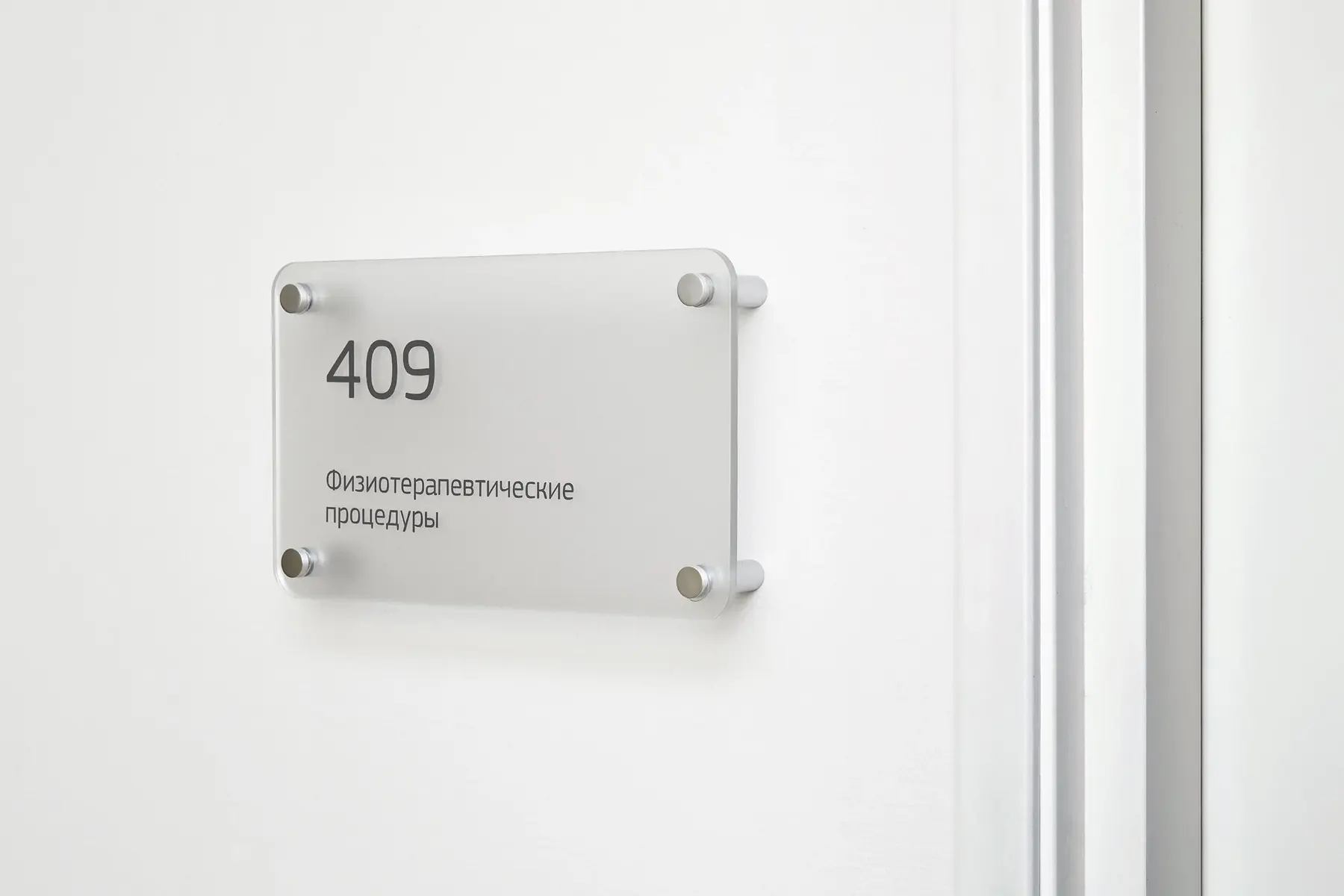 Frosted acrylic room number plate mounted with four silver standoffs on white wall