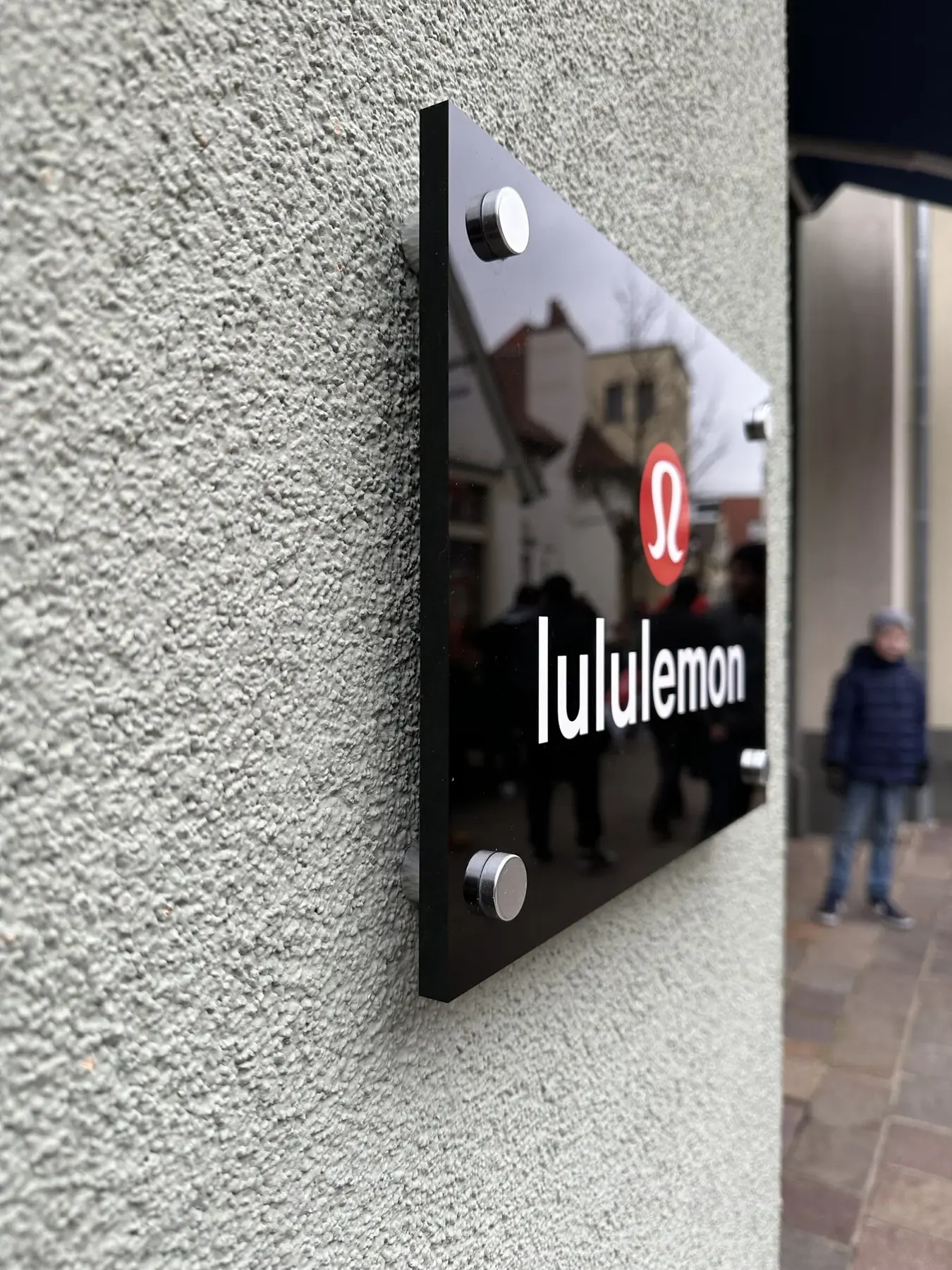 Lululemon retail store exterior with black acrylic sign mounted on silver standoffs